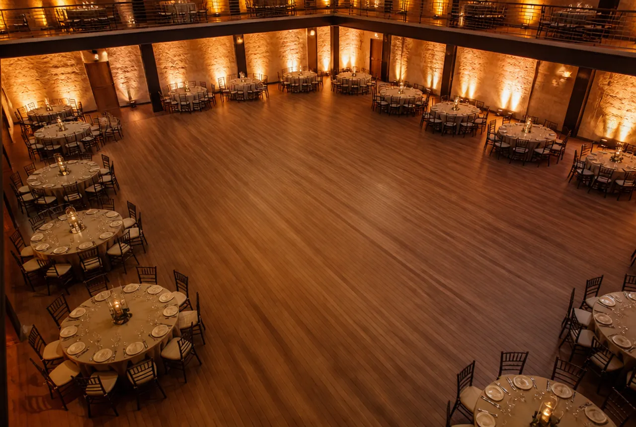 Banquet tables set around the perimeter of a hall leaving a large open centre floor with warm uplighting.