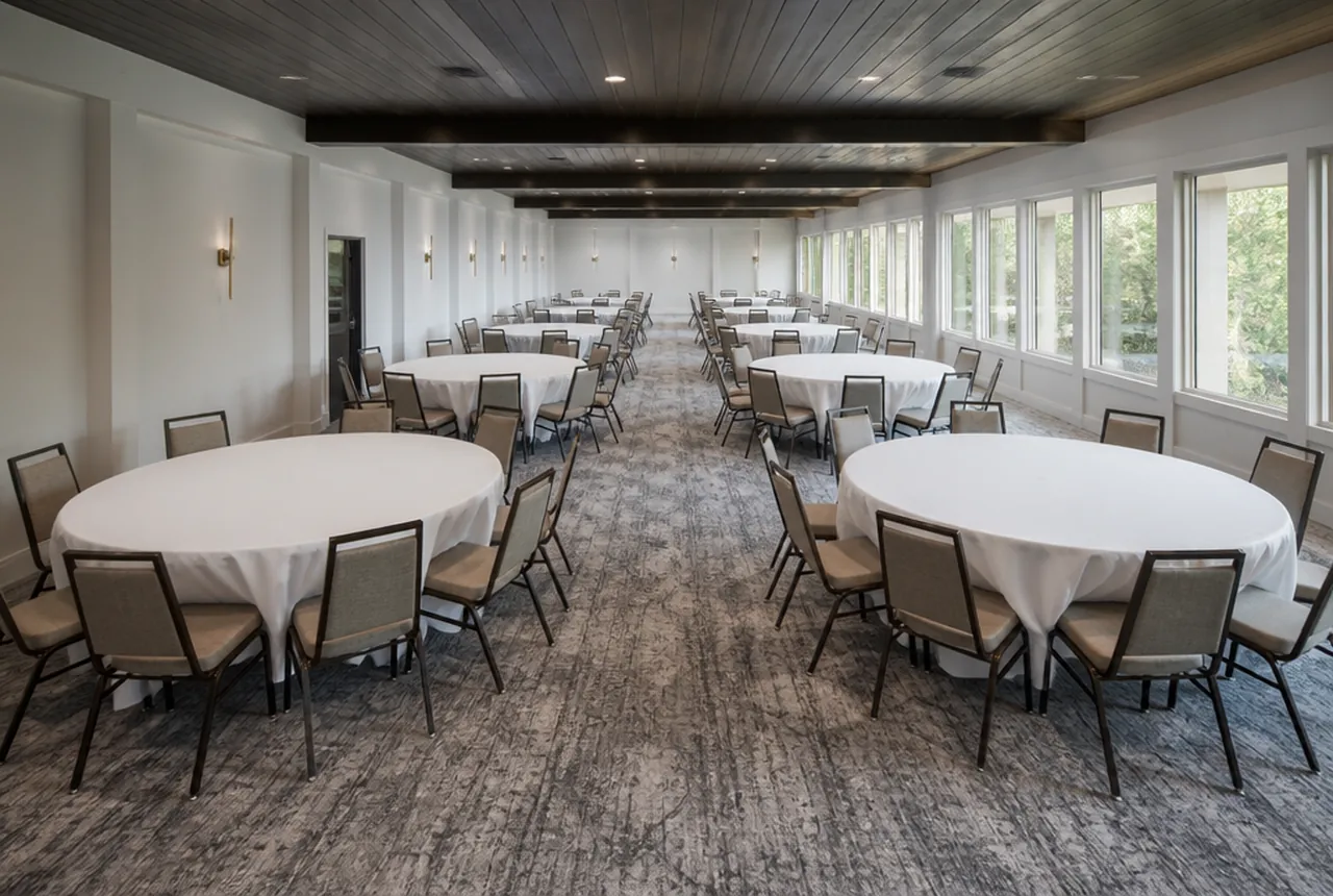 A long narrow function room set with 60-inch round tables in two columns, windows down one side and daylight.