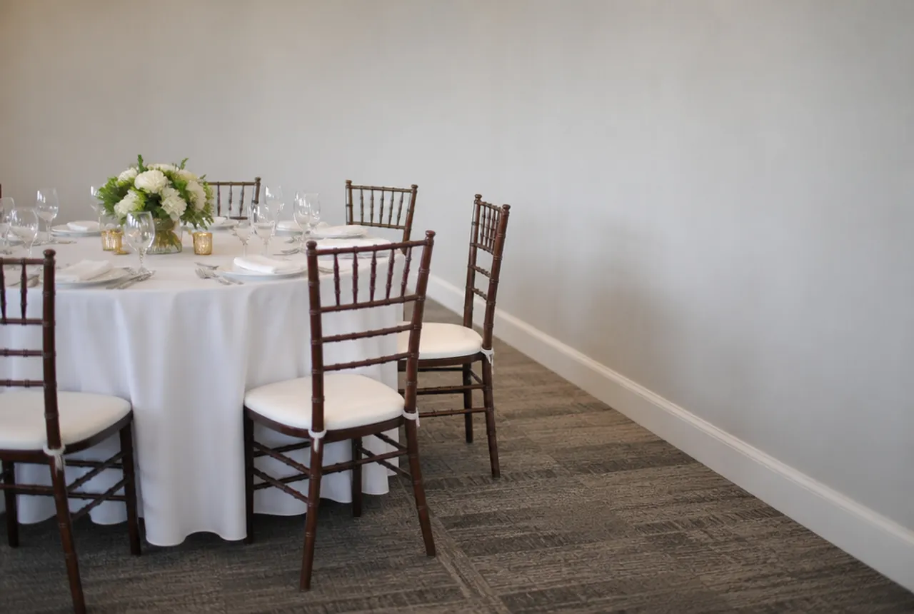 A dressed round table set close to a plain painted wall with a clear walking strip between the chair backs and the wall with soft light.