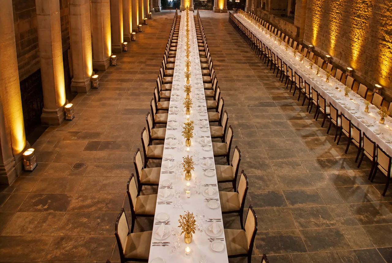 Long imperial king's tables run end to end down the length of a room with guests seated on both sides