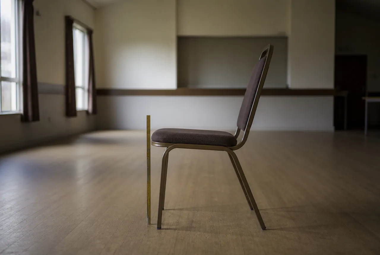 A single stacking banquet chair photographed from the side with a folding rule beside it